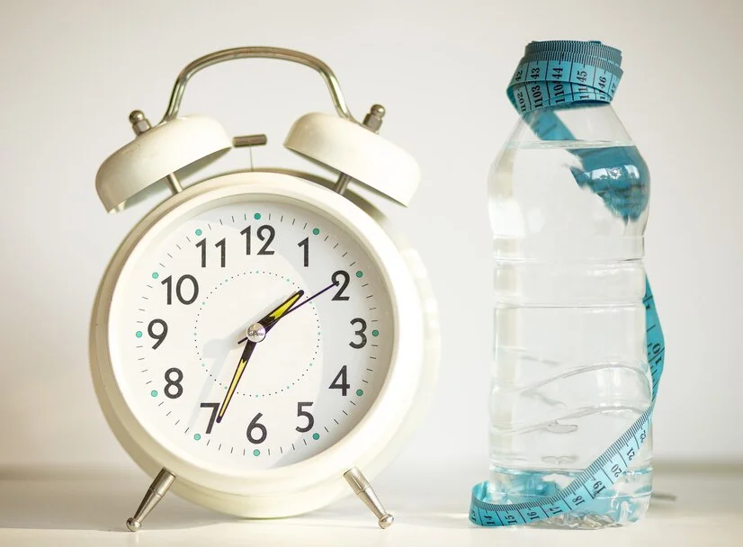 biały zegarek na nóżkach a obok butelka wody z centymetrem krawieckim 