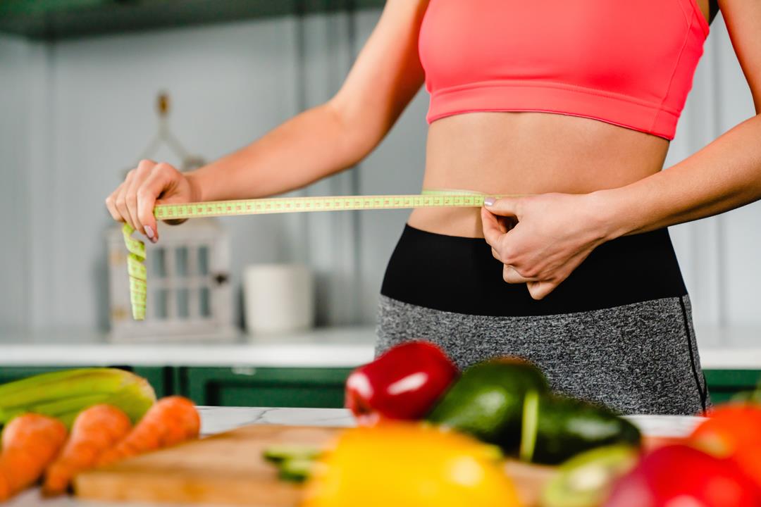 kobieta mierzy swój brzuch centymetrem krawieckim. Stosuje dietę pudełkową i chudnie