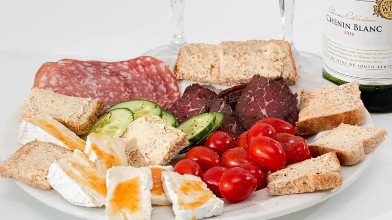 Plasterki szynki i kiełbasy na desce z widocznymi etykietami produktów