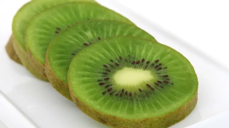 Przekrojone świeże kiwi obok całych owoców na jasnym tle