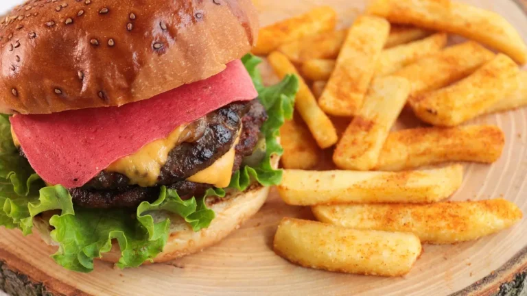 Burger z serem i dodatkami na tacy obok frytek