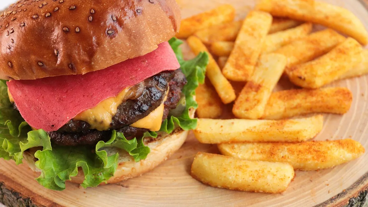 Burger z serem i dodatkami na tacy obok frytek